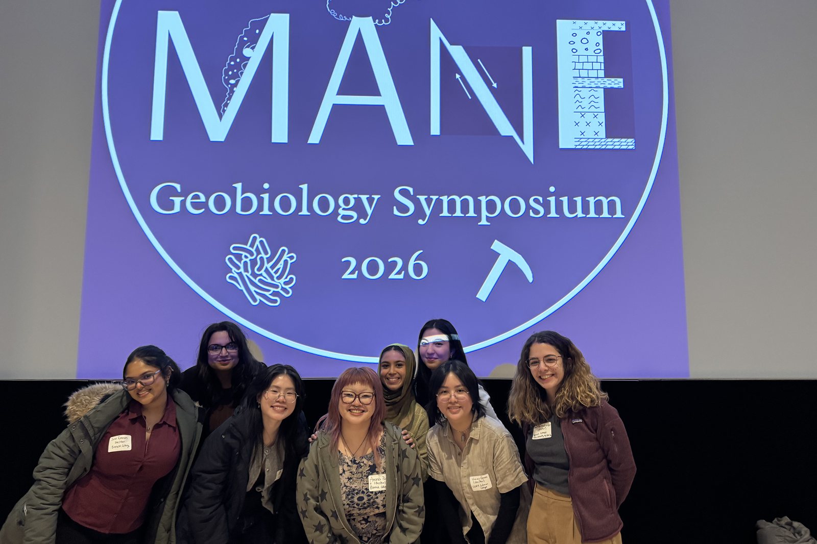 Lab members smiling in front of the MANE Geobiology Symposium 2026 title slide